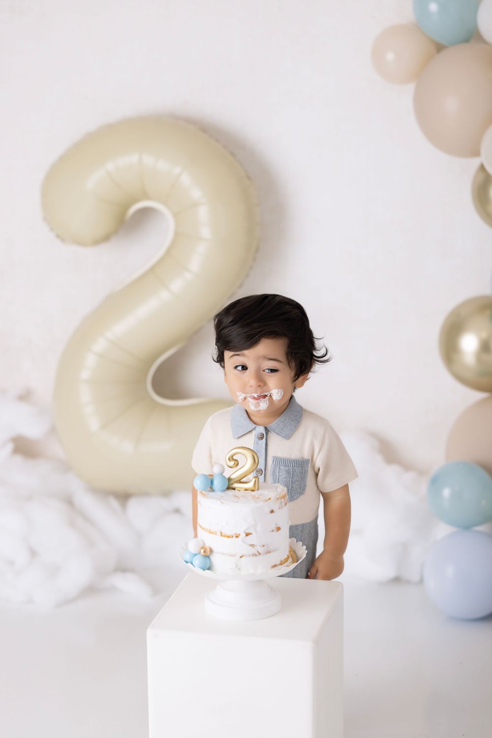 Birthday celebration photo featuring white cake on pedestal with large number 2 balloon and soft blue balloon decorations.