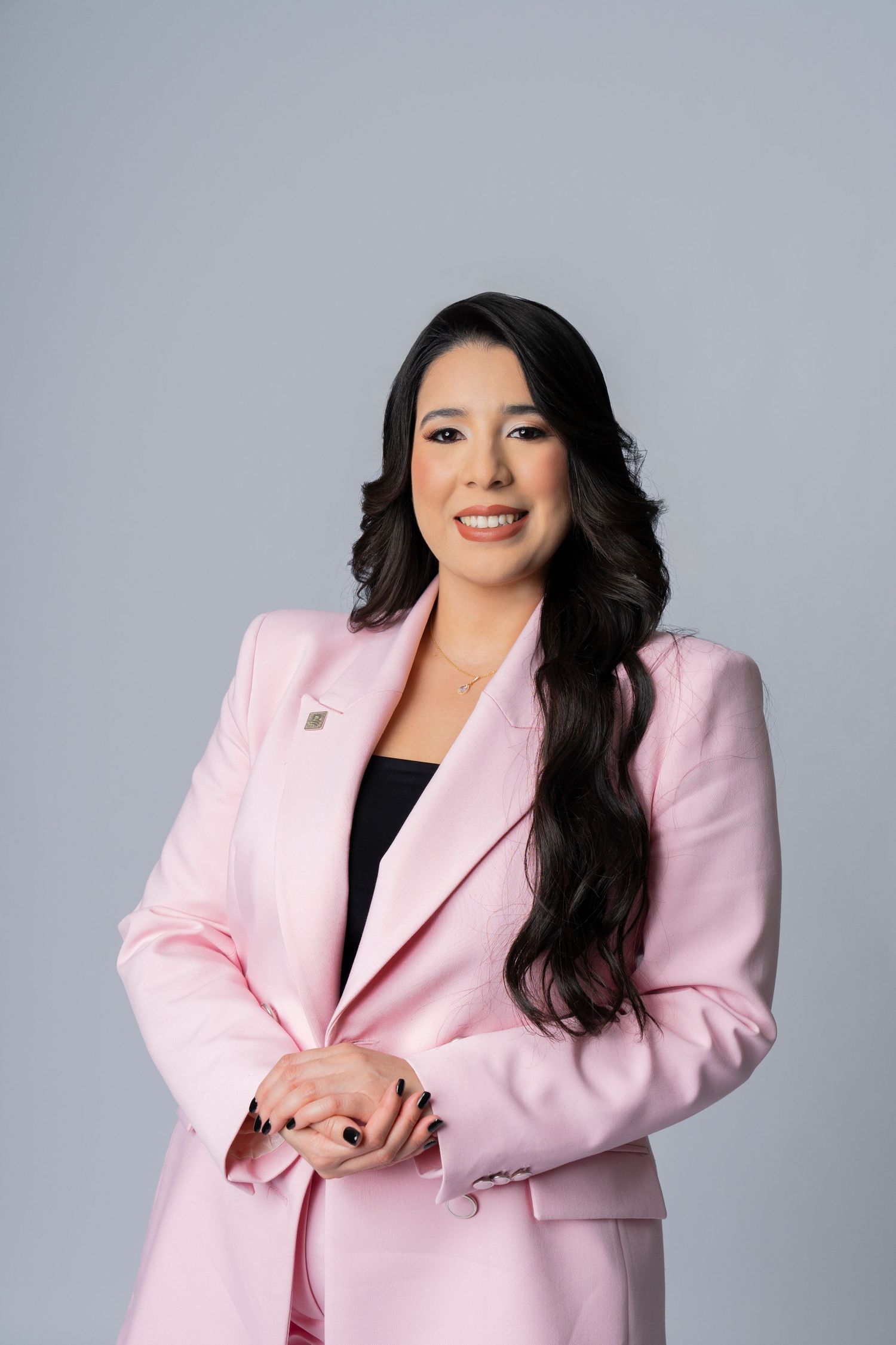 Professional headshot of woman wearing pink blazer against grey background.