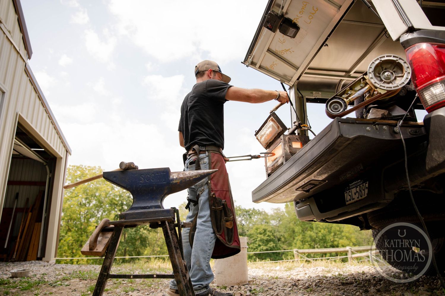 Mobile farrier workshop setup with anvil and tools near pickup truck.