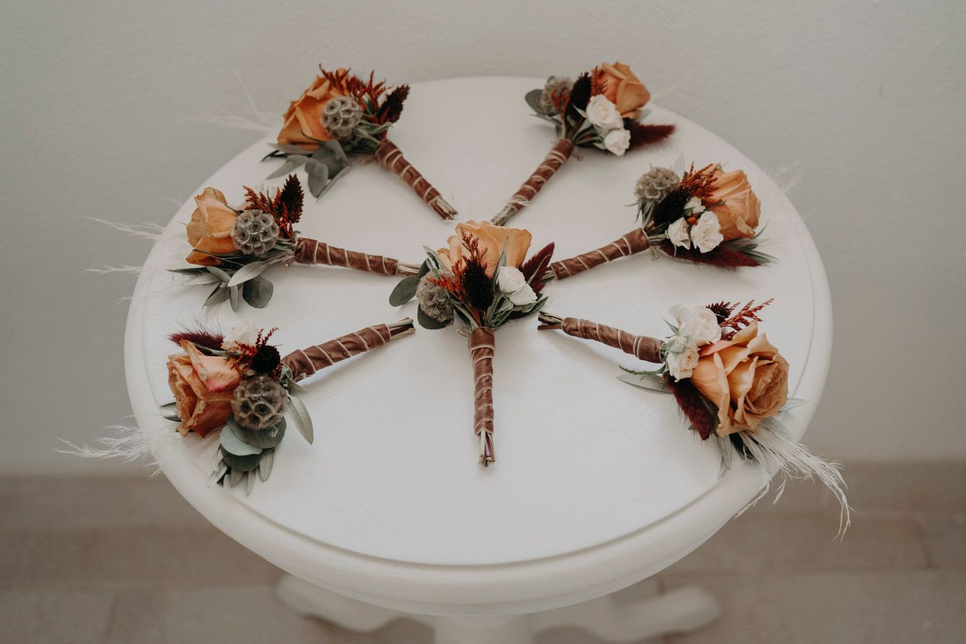 Small peach-colored wedding boutonnieres arranged in a circular pattern on a white surface.