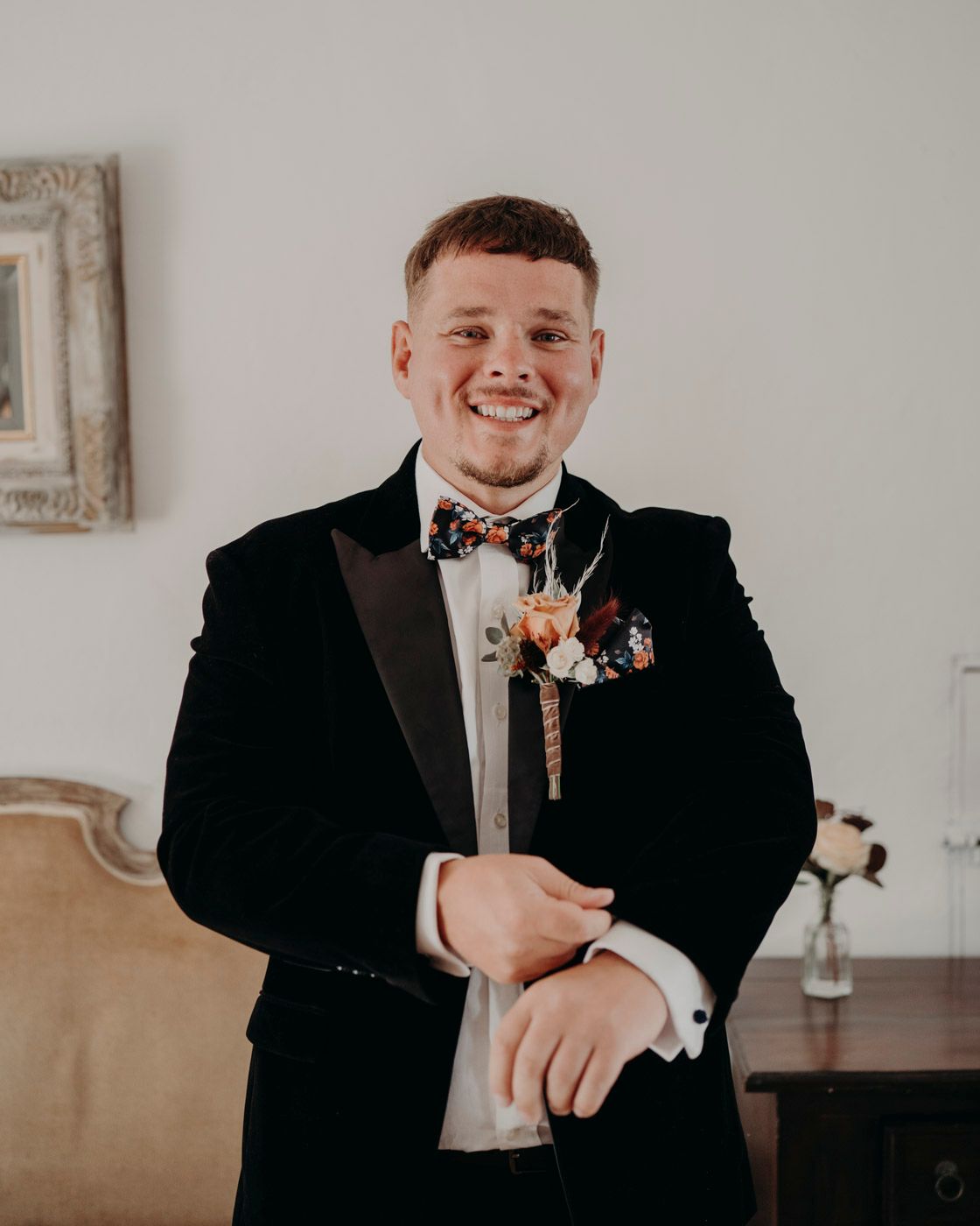 A smiling person in a black tuxedo with bow tie and boutonniere poses during a formal occasion.