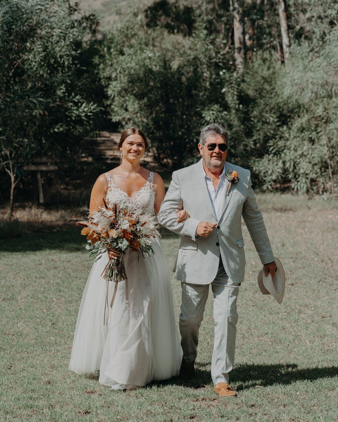 Two wedding attendees walking arm-in-arm outdoors, with the bride carrying a beautiful autumnal bouquet.