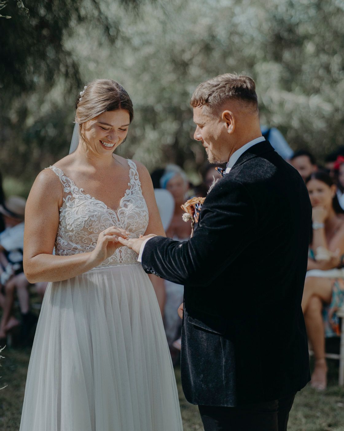A bride and groom share a joyful moment during their outdoor wedding ceremony as they exchange rings.