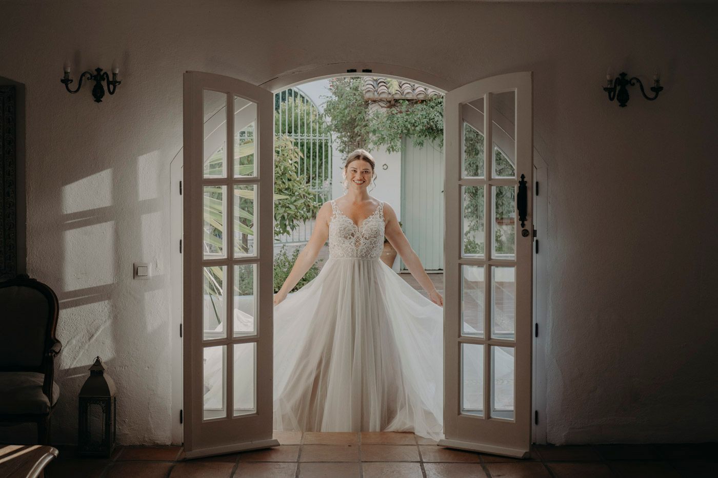 A flowing wedding dress is illuminated in a doorway with French doors casting dramatic shadows.