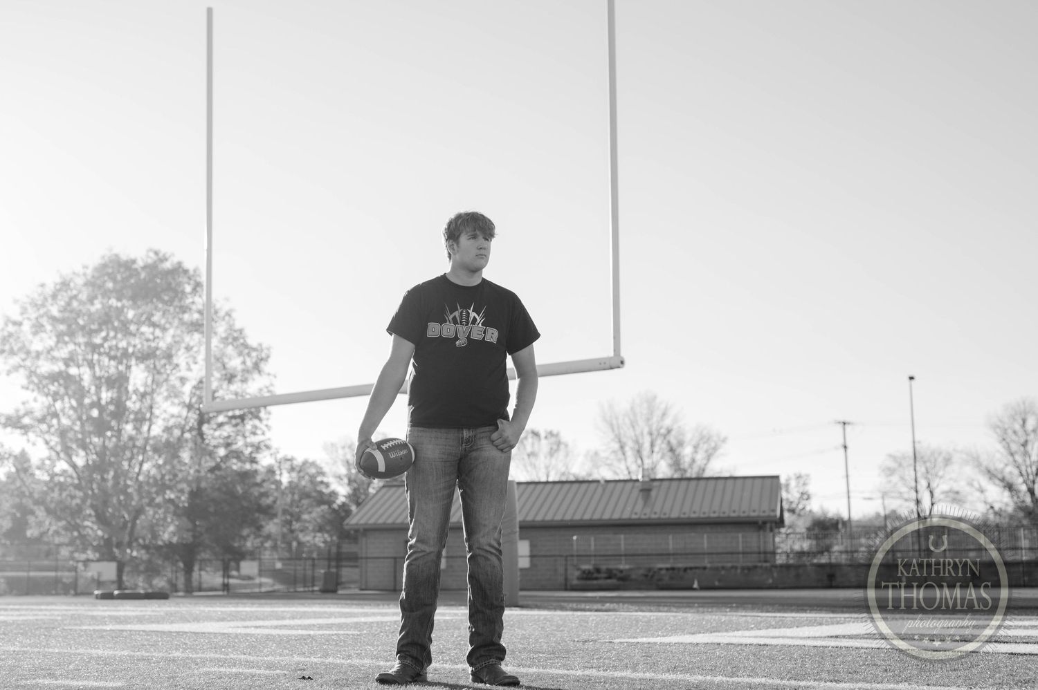 Black and white photo of person standing on football field with goalpost in background.