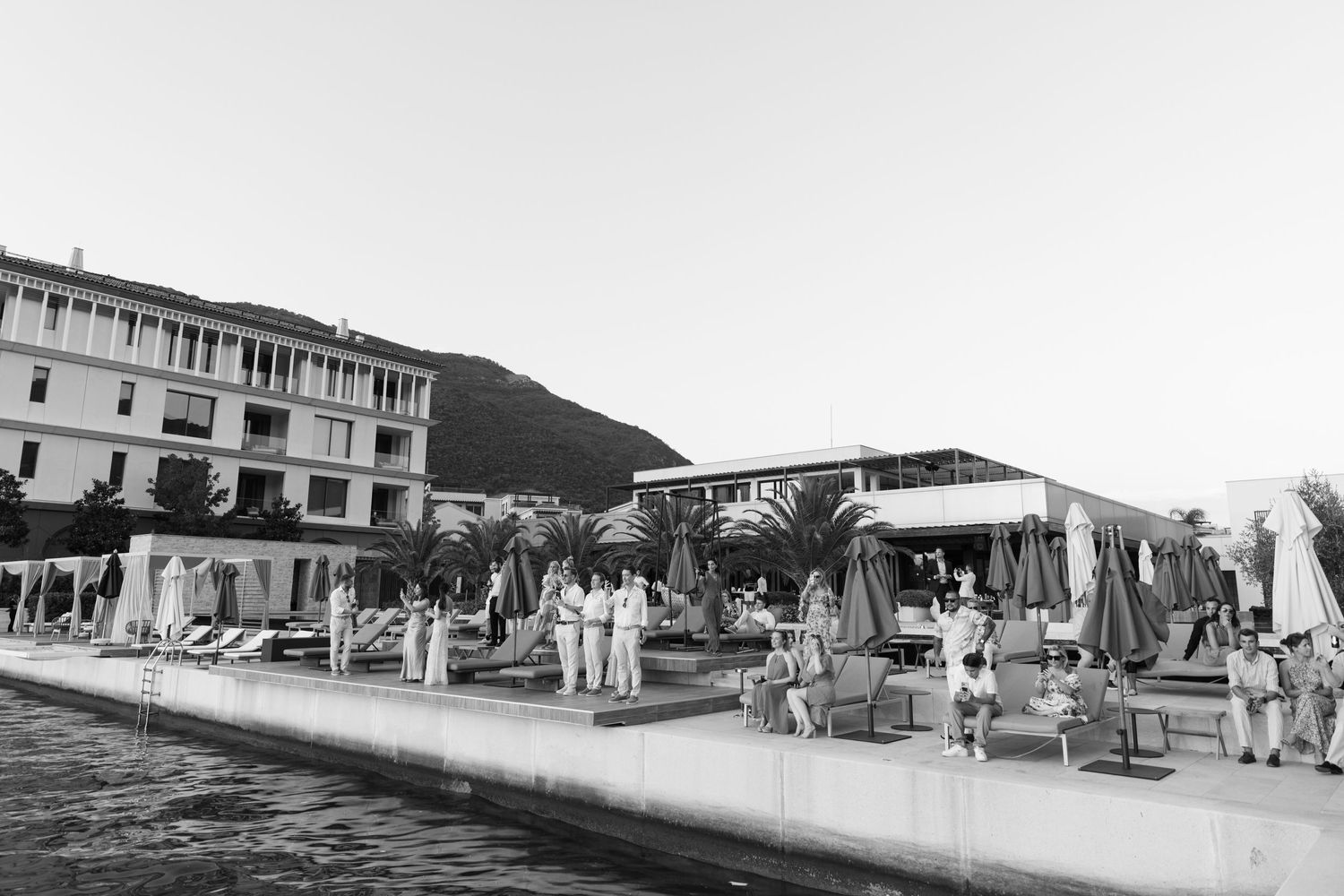 Vintage black and white photo showing beachgoers and umbrellas along a coastal resort promenade in a tropical setting.