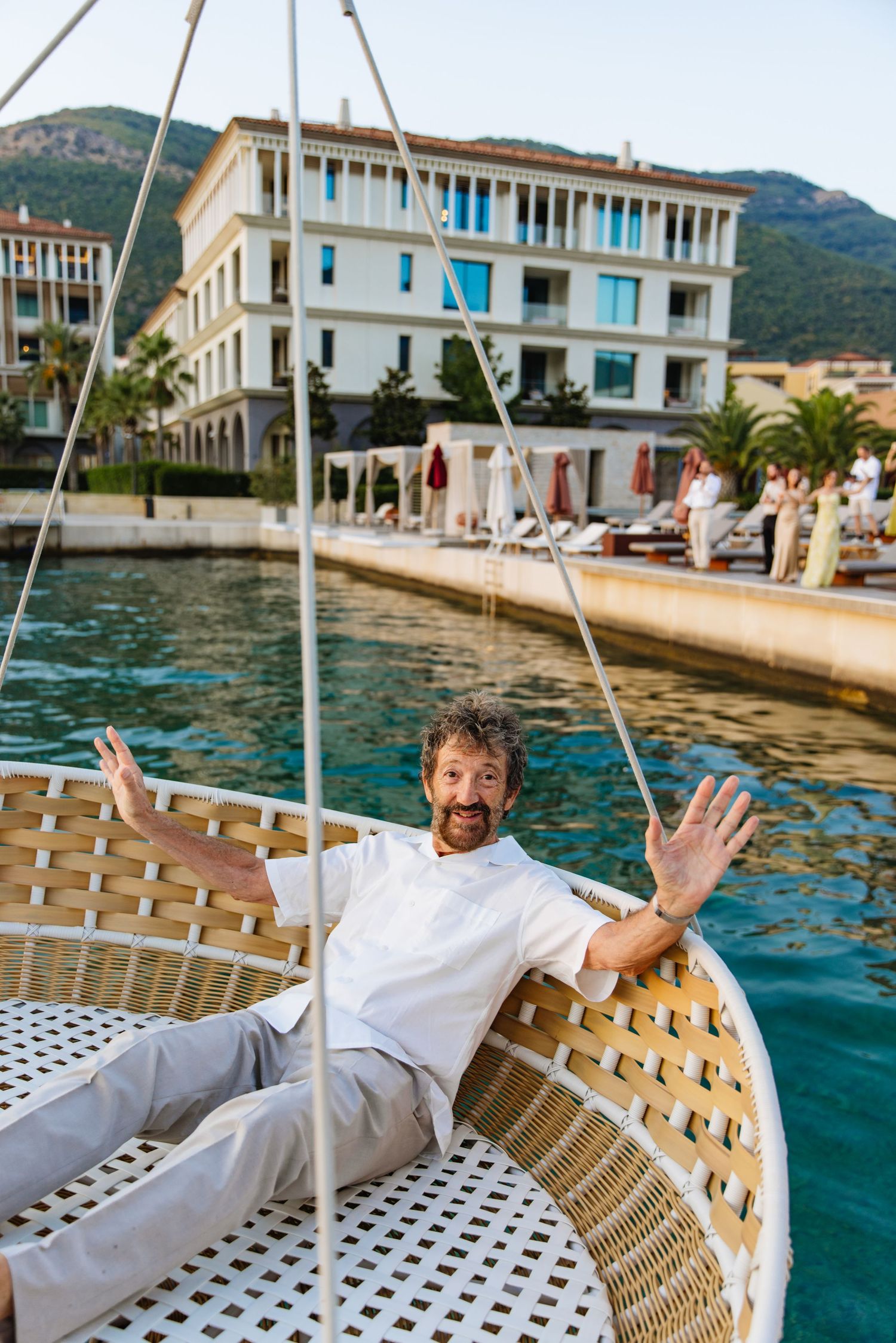 Person enjoying a relaxing day on a woven lounge chair by the waterfront promenade in a Mediterranean coastal town.