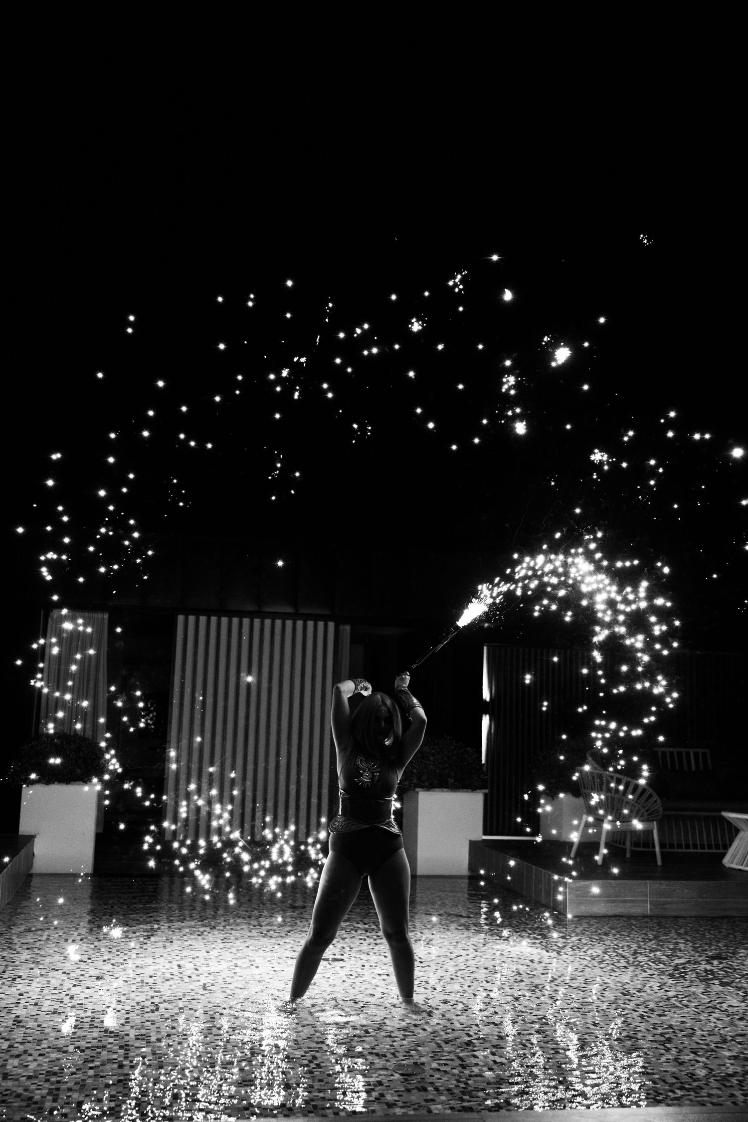 A silhouetted performer stands in a dramatic display of sparkling pyrotechnics and lights against a dark background.