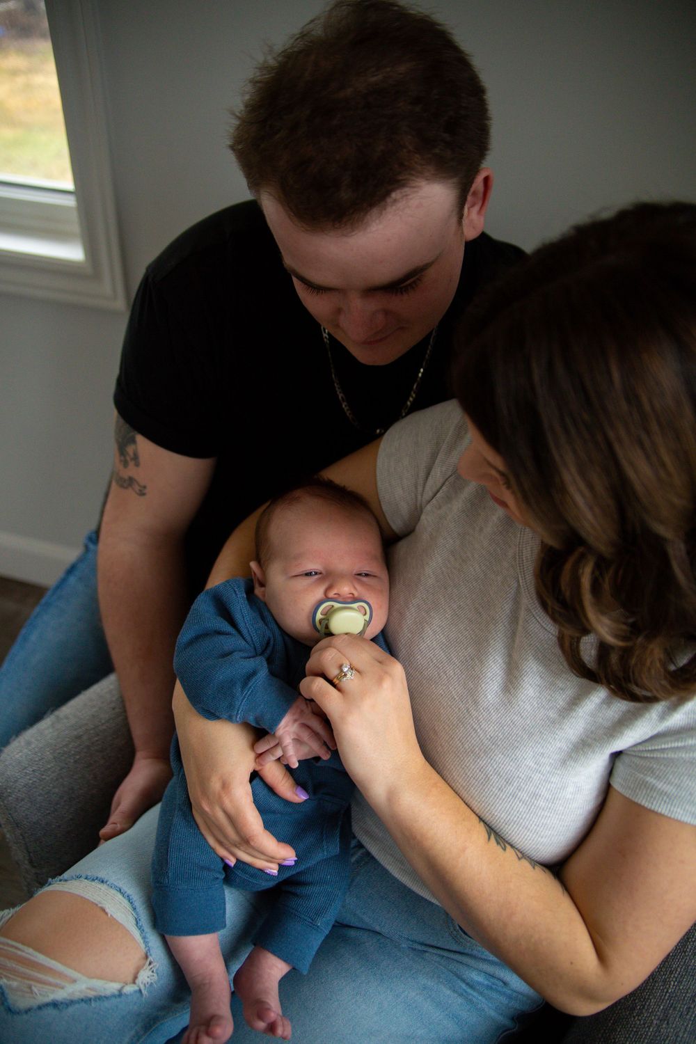 Baby with pacifier being comforted by caregivers on grey couch.