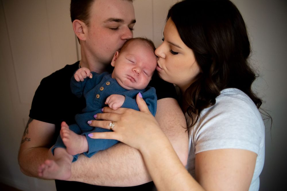 Parents share tender kisses with their sleeping baby in an intimate portrait.