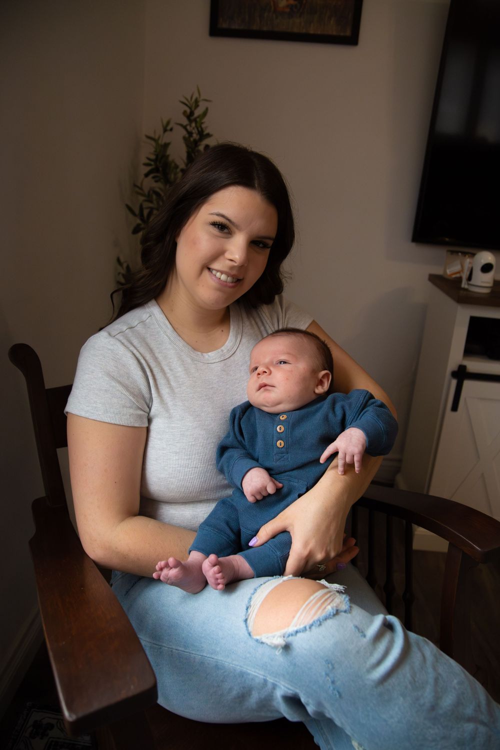 Parent holding smiling infant wearing blue outfit while sitting at wooden table.