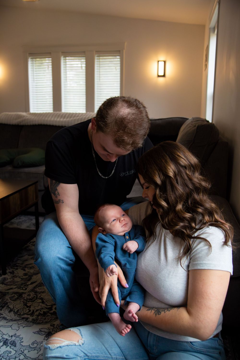 An intimate family portrait showing parents gazing lovingly at their infant in blue clothing.