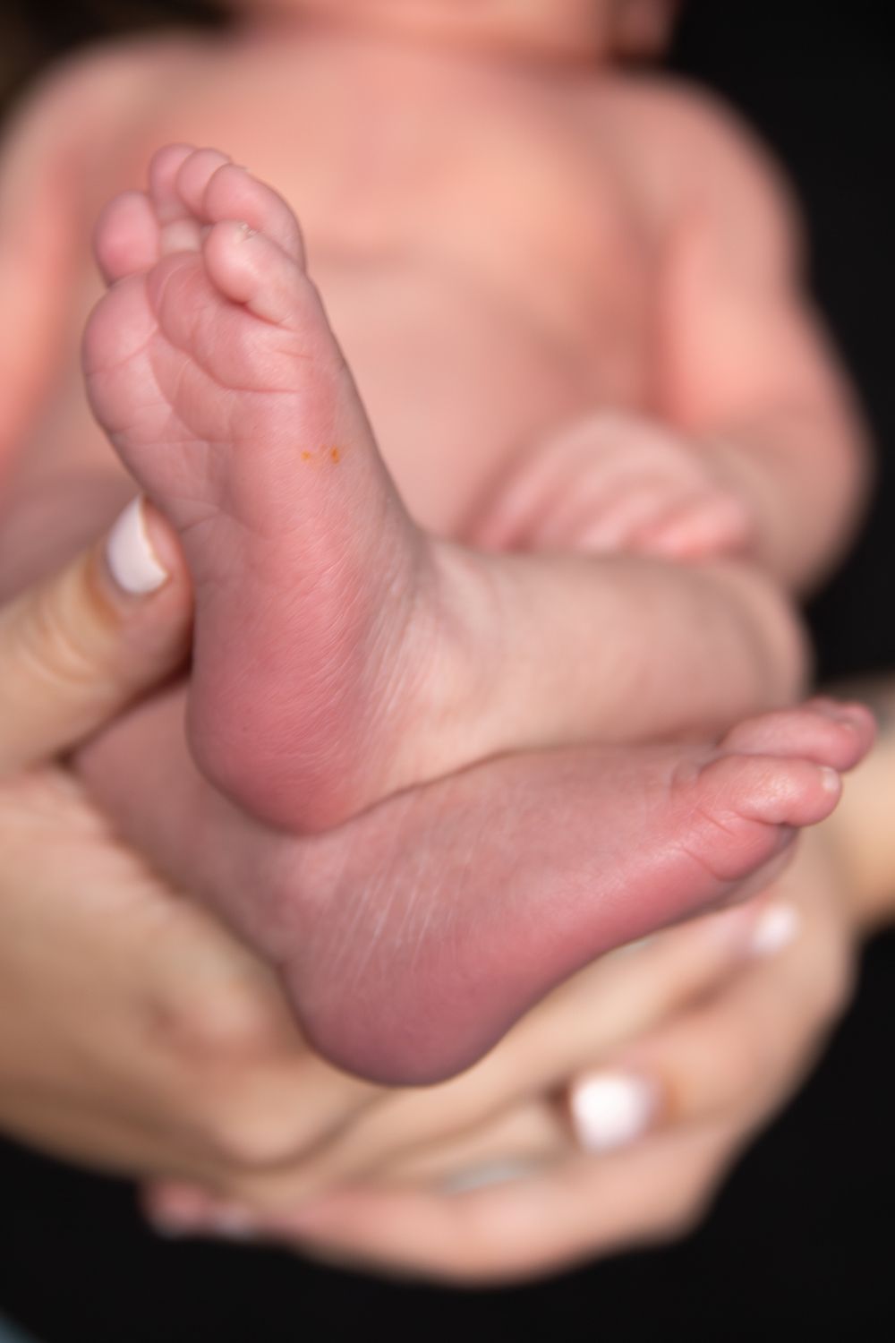 Close-up series of a baby's tiny feet being gently cradled in adult hands against a dark background.