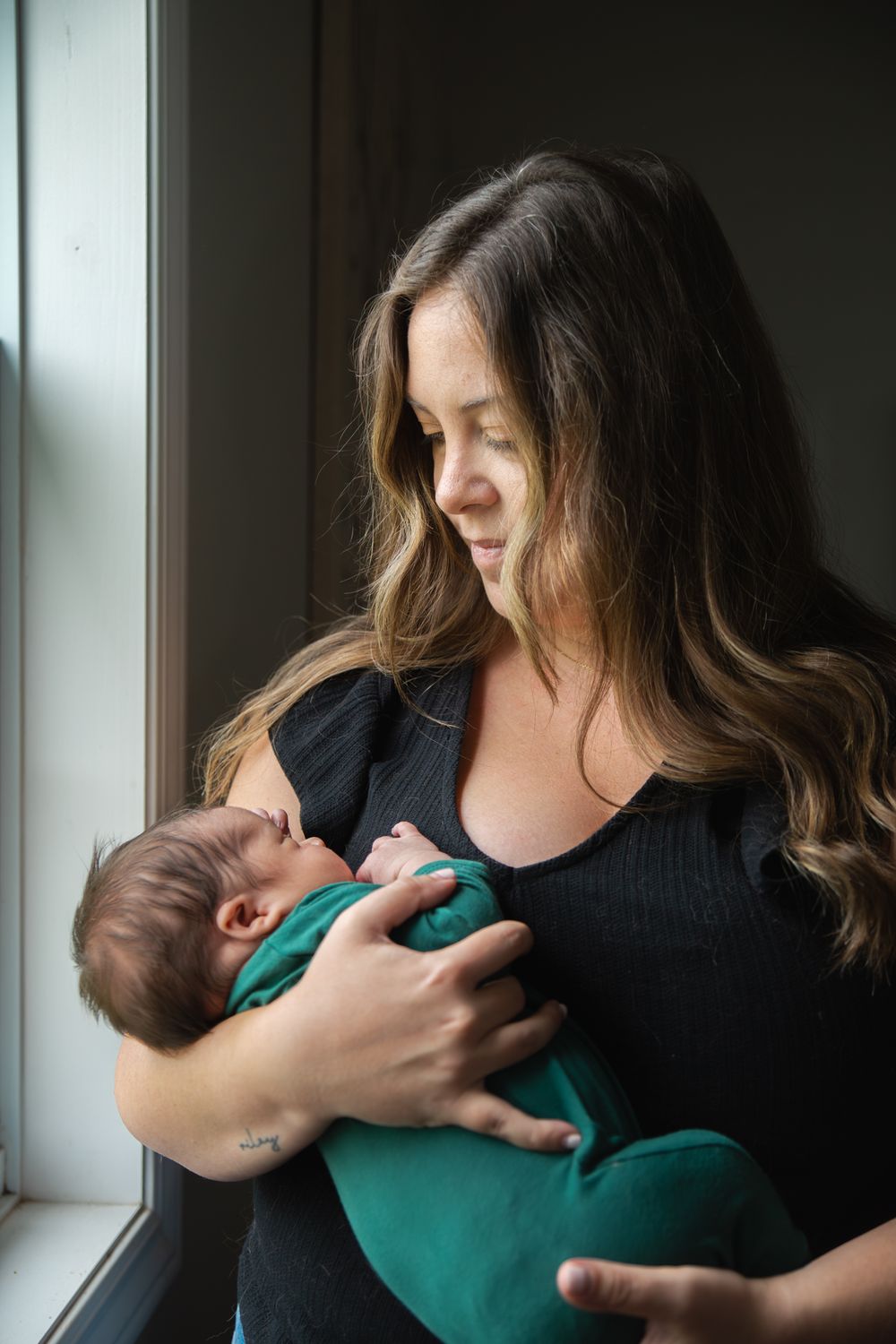 A sequence of nurturing moments between caregiver and infant wearing green by a bright window.
