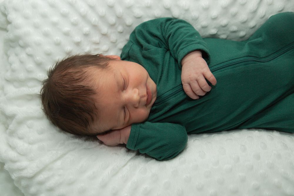 A baby in green sleepwear resting peacefully on white textured bedding.