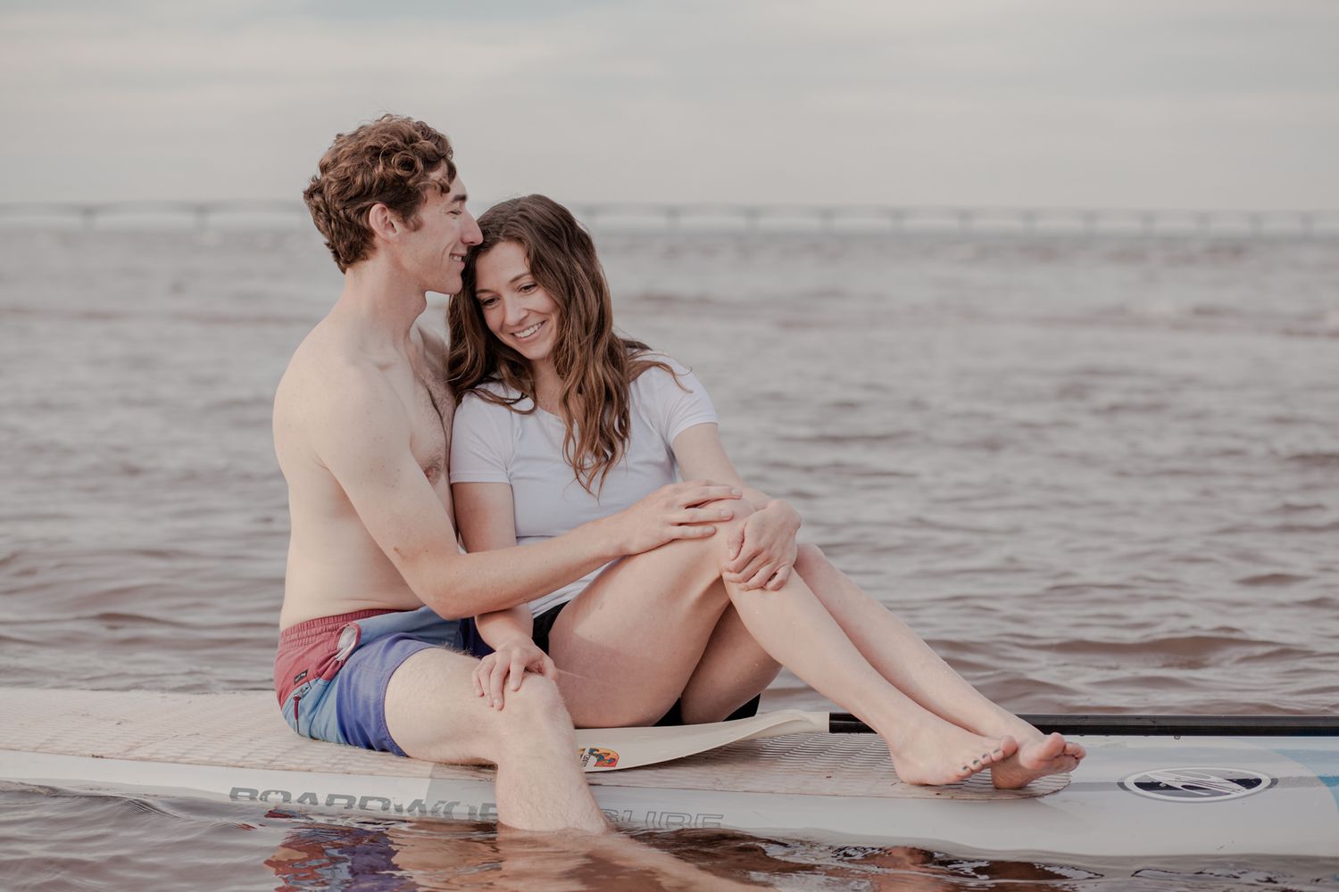 Couple sitting together on a paddleboard during a free cinematic couples photoshoot in Prince Edward Island. Lumenali Photography.