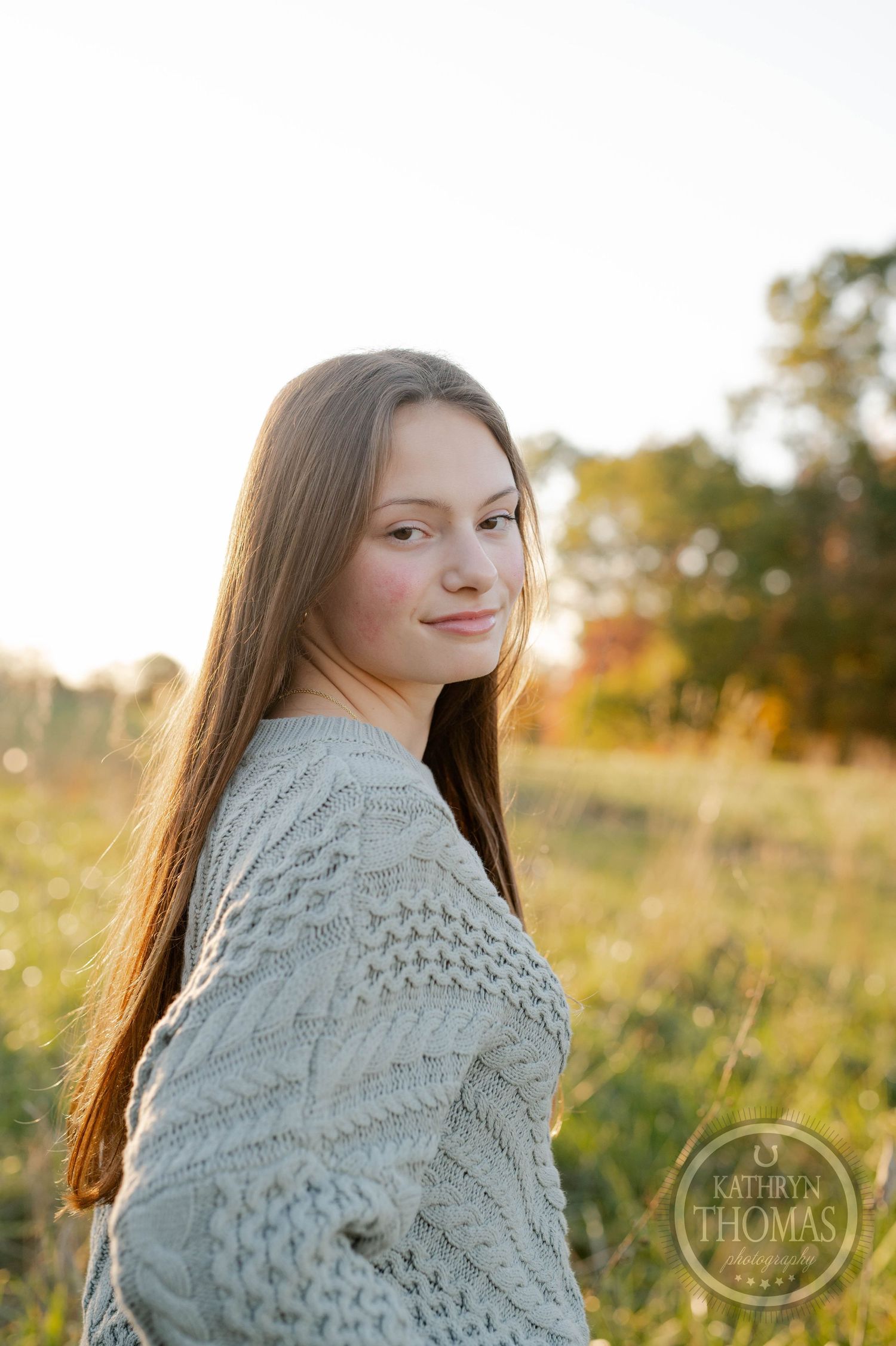 Soft golden hour portrait of someone in a detailed cable knit sweater against autumn foliage.