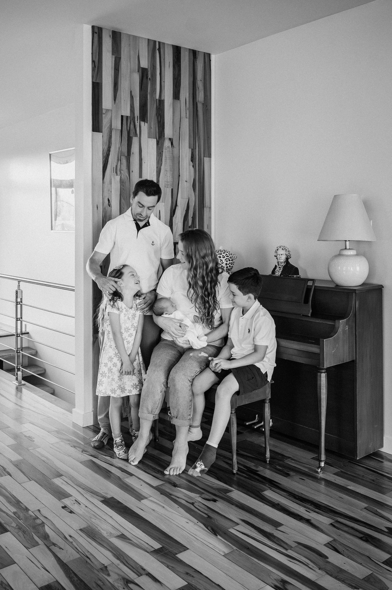 Family gathered around piano in modern home with striking wooden floor pattern.