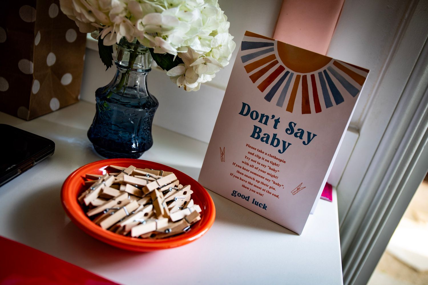 Wedding decor with white flowers in blue vase next to plate of snacks and 'Hey Baby' book.