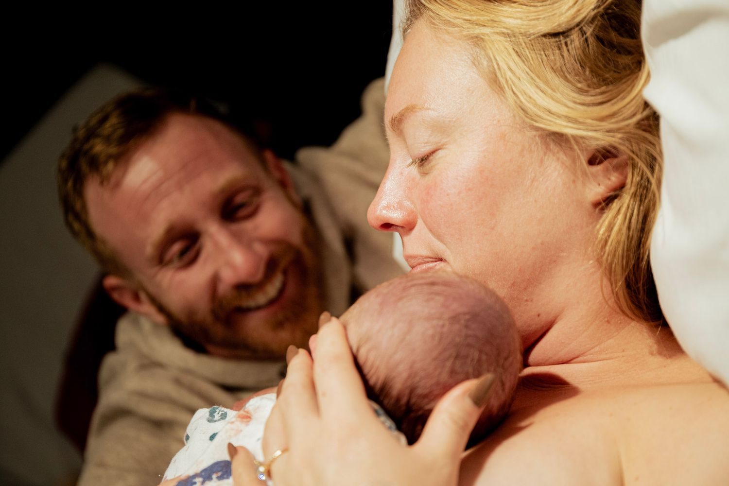 New parents share a tender moment with their newborn baby in hospital after birth.