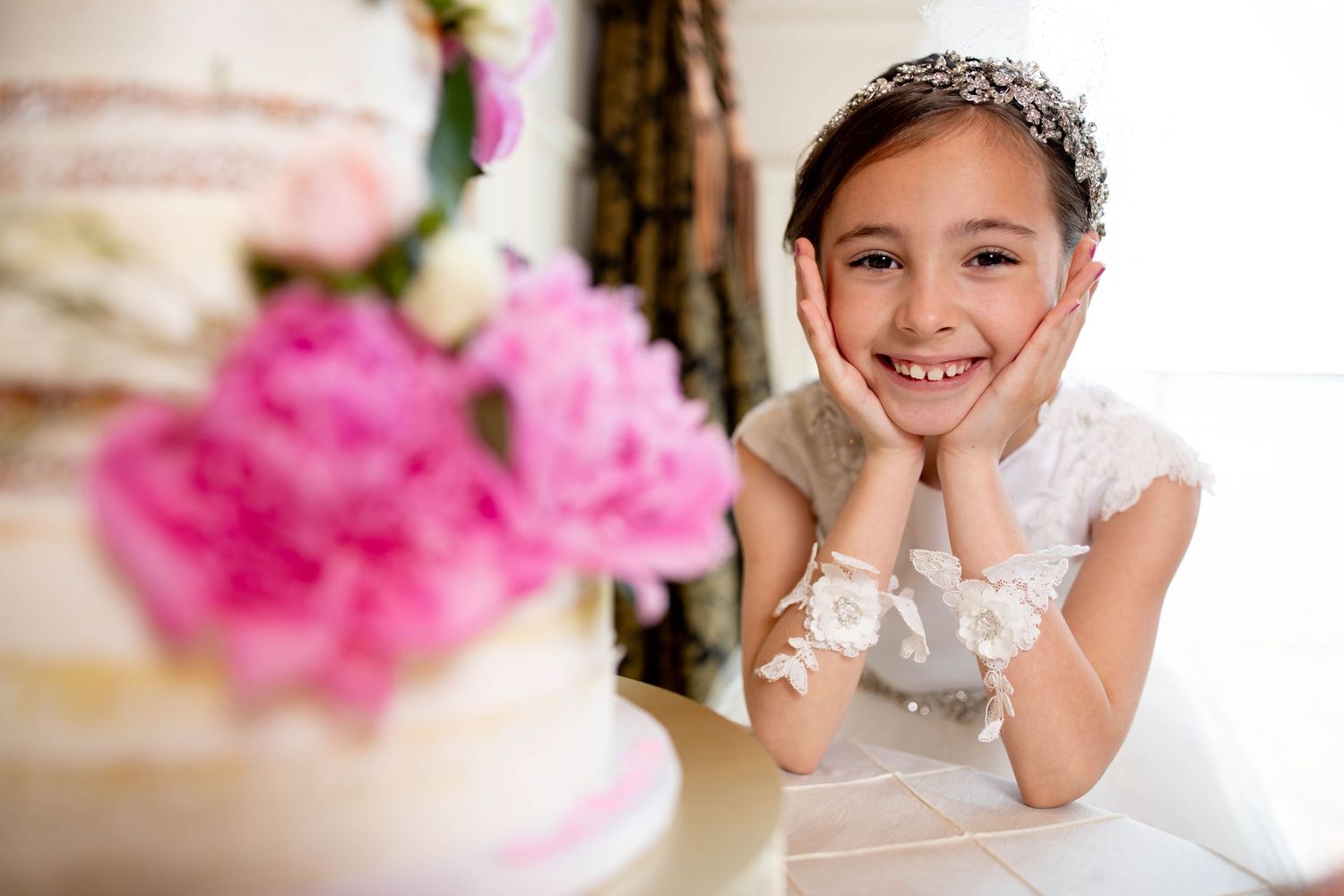 Young girl in white dress smiles while looking at pink flower decorations.