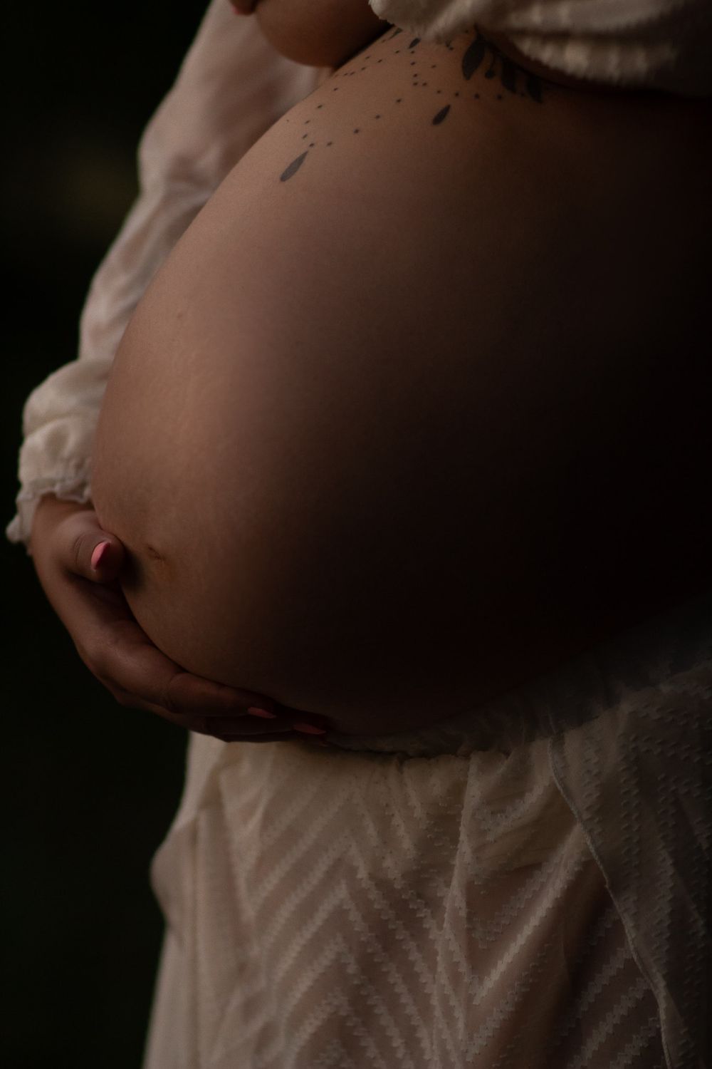 close up of a pregnant belly with tattoo and mother's hands