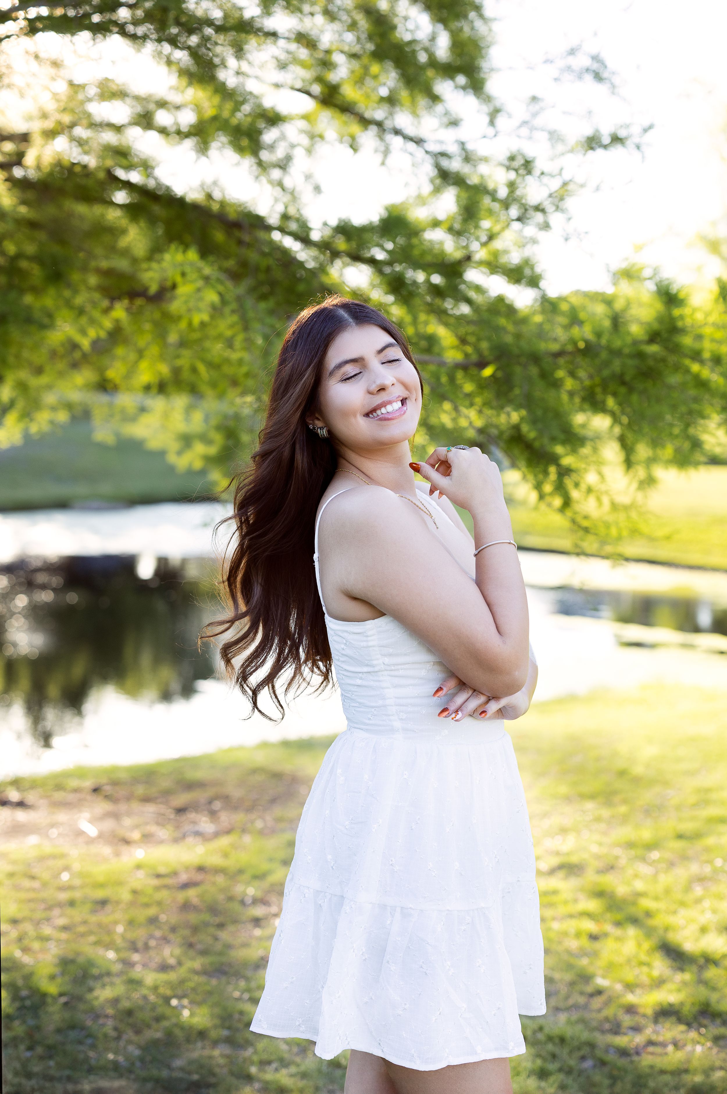 A serene summer portrait in a white dress by a pond with lush greenery and sunlit scenery in the background.