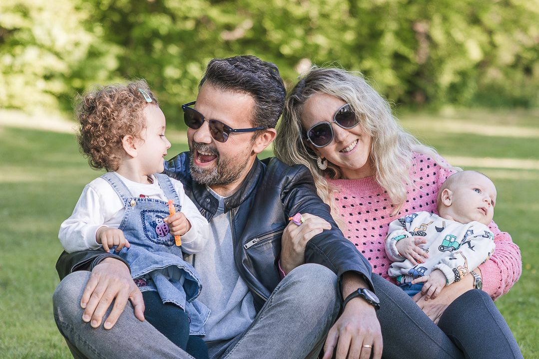 A loving family relaxes together on a blanket in a sunny park during a warm afternoon.