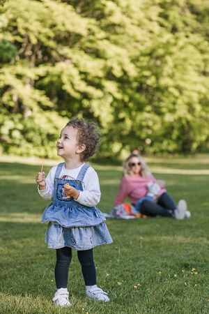 A small child in a denim jacket plays on a sunny grassy lawn while looking upward with wonder.