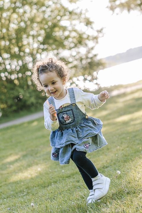 Child in denim overalls runs energetically across sunny grass.