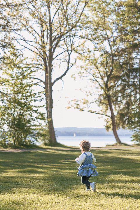 Small figure runs across sloping grass towards trees with water view in background.