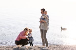Family members interact playfully on a beach at sunset with geese swimming in the background.