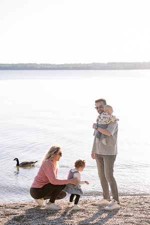 A family plays and explores together along a peaceful lakeside beach at sunset.