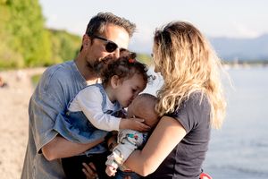 Family members share a playful moment by a waterfront on a sunny day.