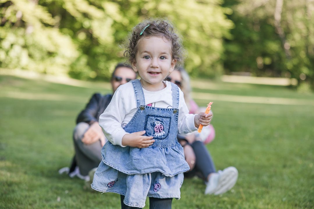 A toddler in denim overalls runs playfully through a grassy park.