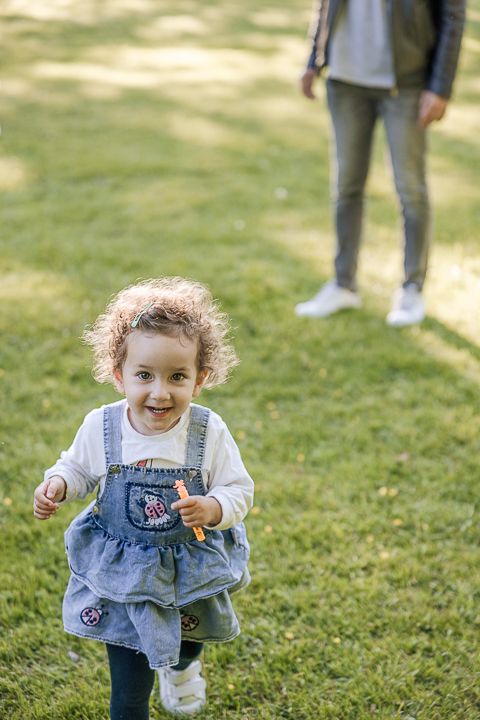 Small child in denim overalls laughs while playing on green grass.