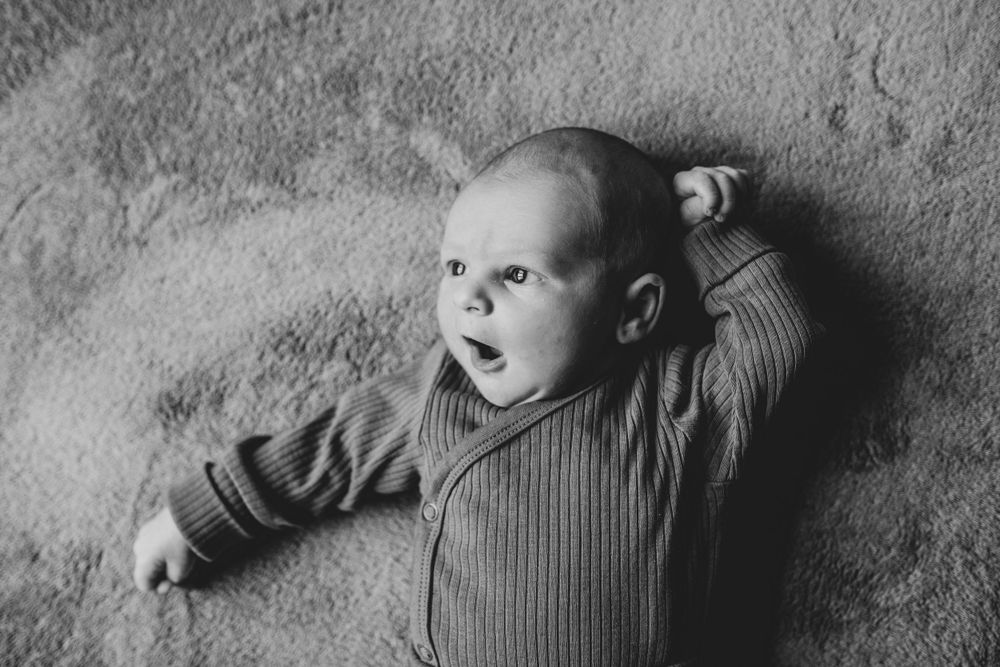 Black and white photo of an infant lying on a textured surface wearing a ribbed onesie.