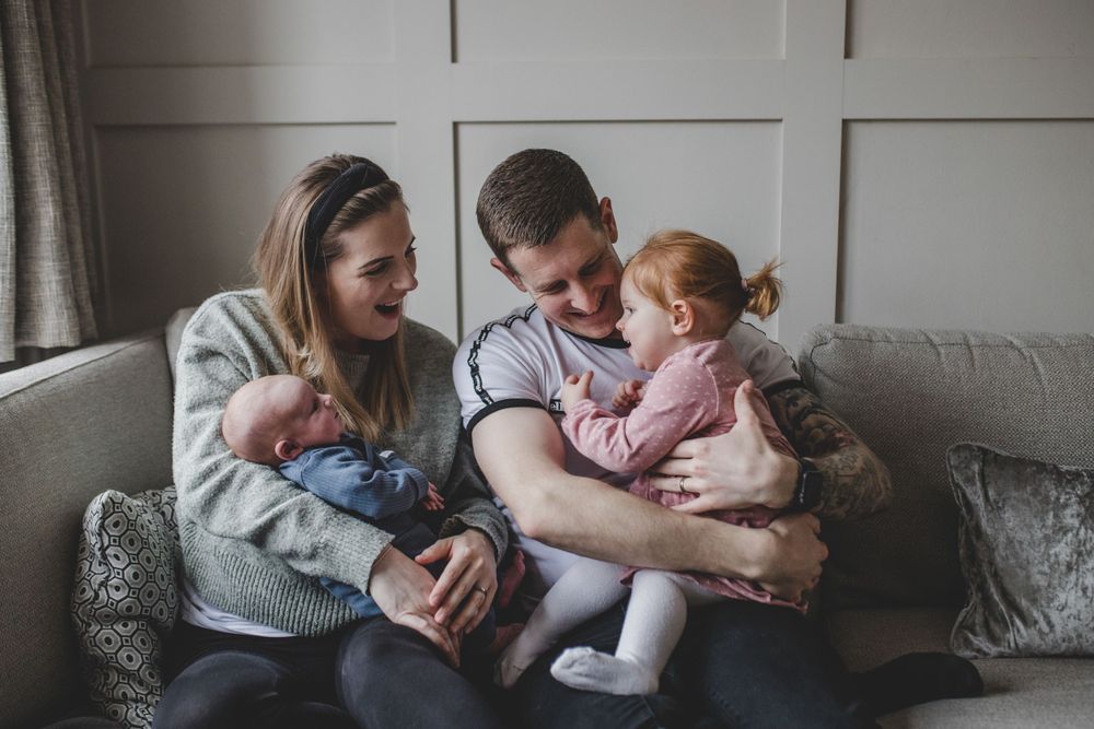A family sits together on a gray couch in a cozy living room, sharing a tender moment at home.