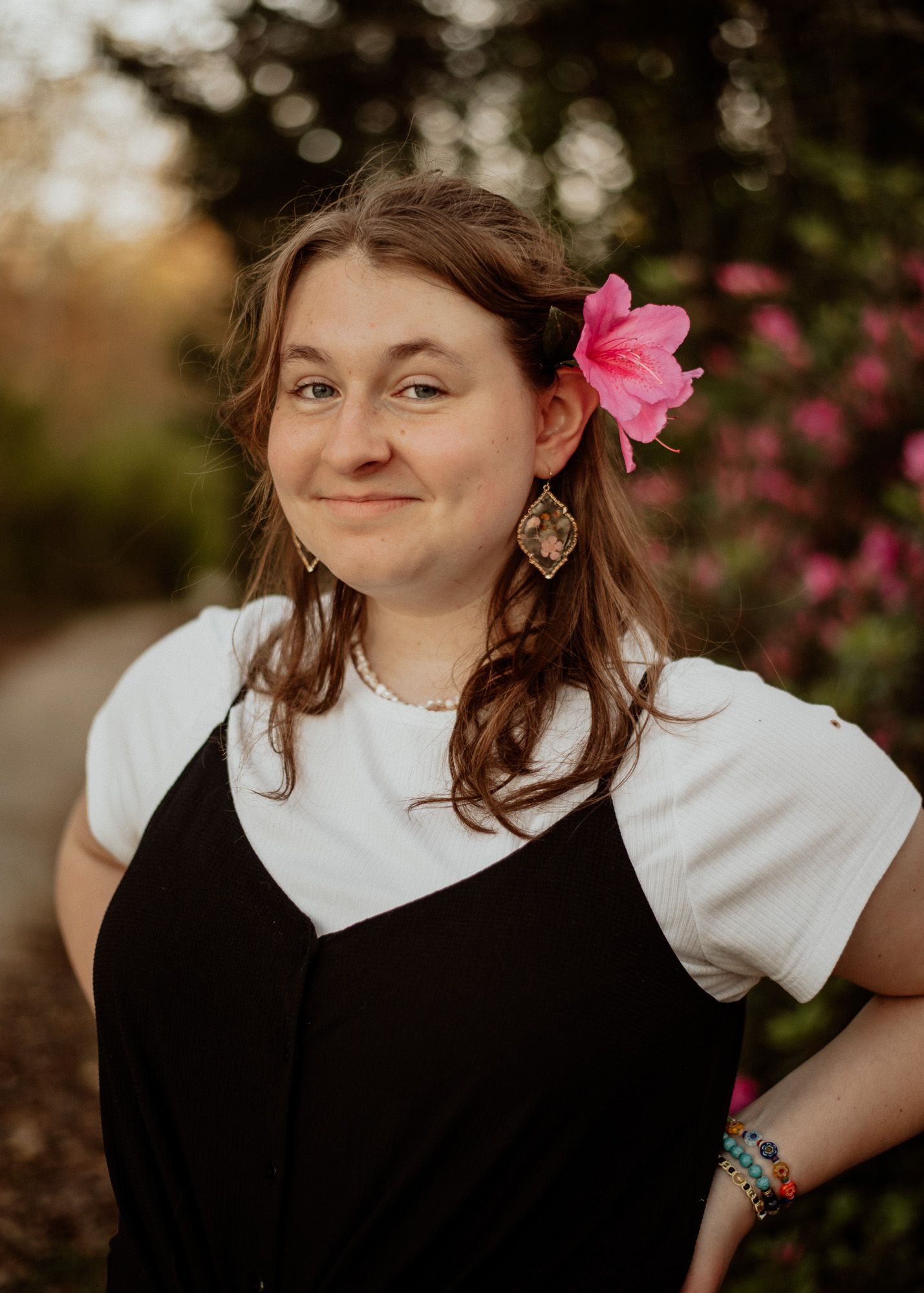 Portrait among pink flowers with a white shirt and black dress.