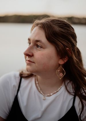 Portrait by a lake wearing pearl necklace and white shirt with black dress.