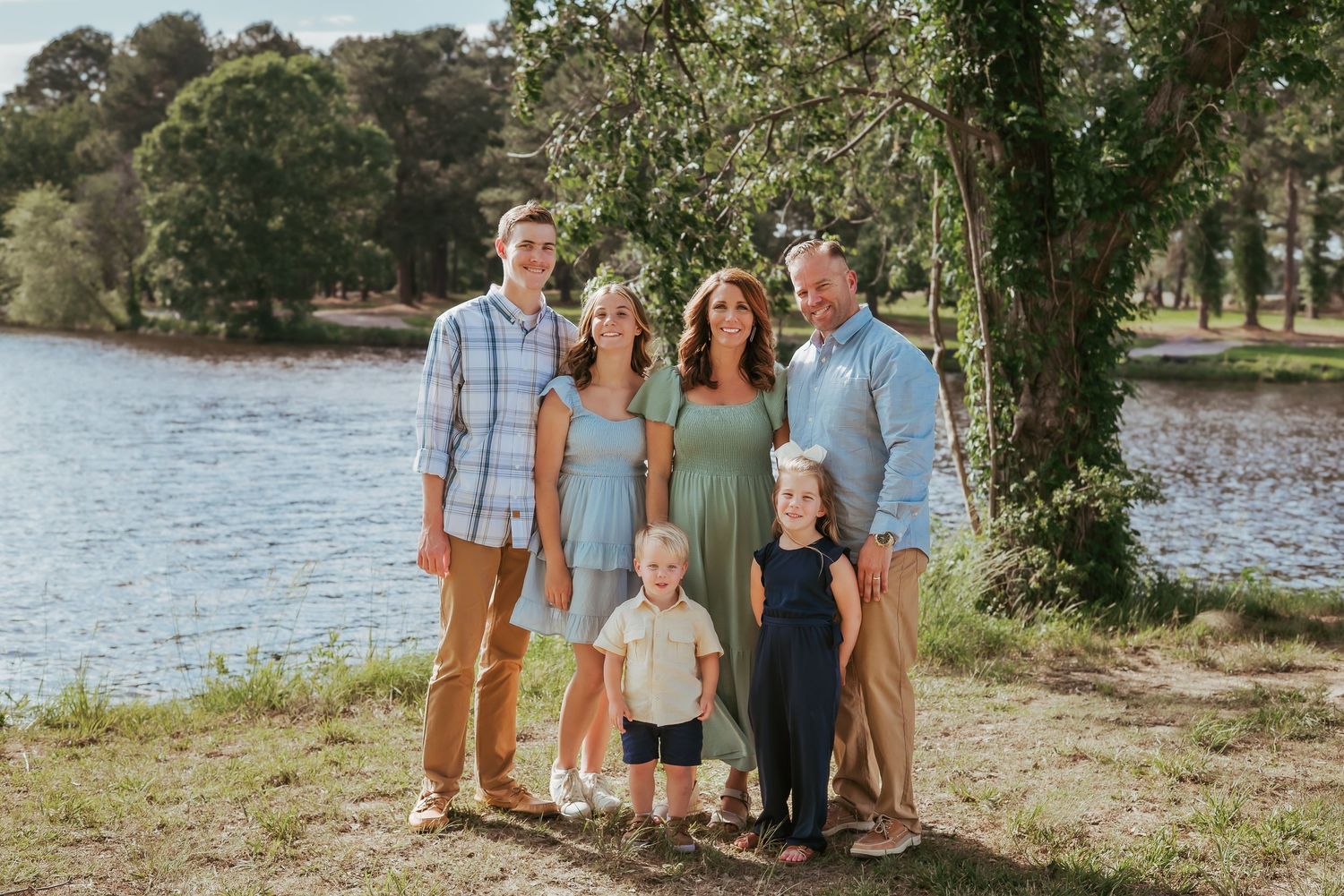 Casual family portrait by a lake with trees in the background.