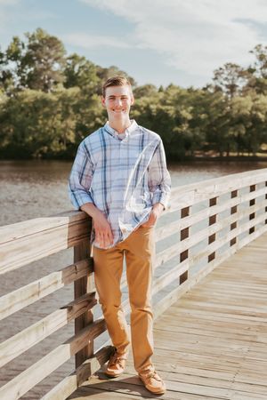 Young person in plaid shirt poses casually on wooden boardwalk during outdoor photo session.