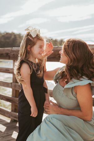 Mother and daughter share a tender moment together on a wooden deck during sunset.