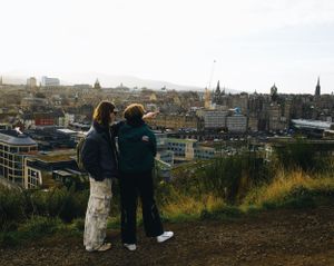 Two people look out over Edinburgh's historic cityscape at dusk from Calton Hill viewpoint.