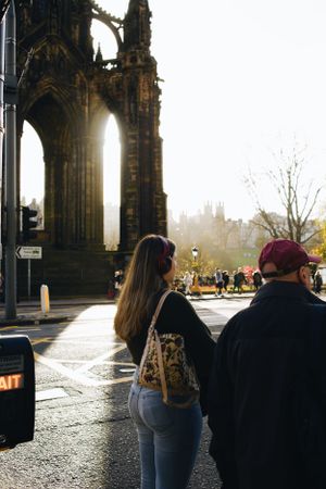 Two people stand near the Gothic arches of Edinburgh's Scott Monument on a sunny afternoon with sunlight streaming through.