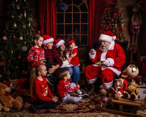 Children in red sweaters gather around Santa Claus in a cozy Christmas setting.