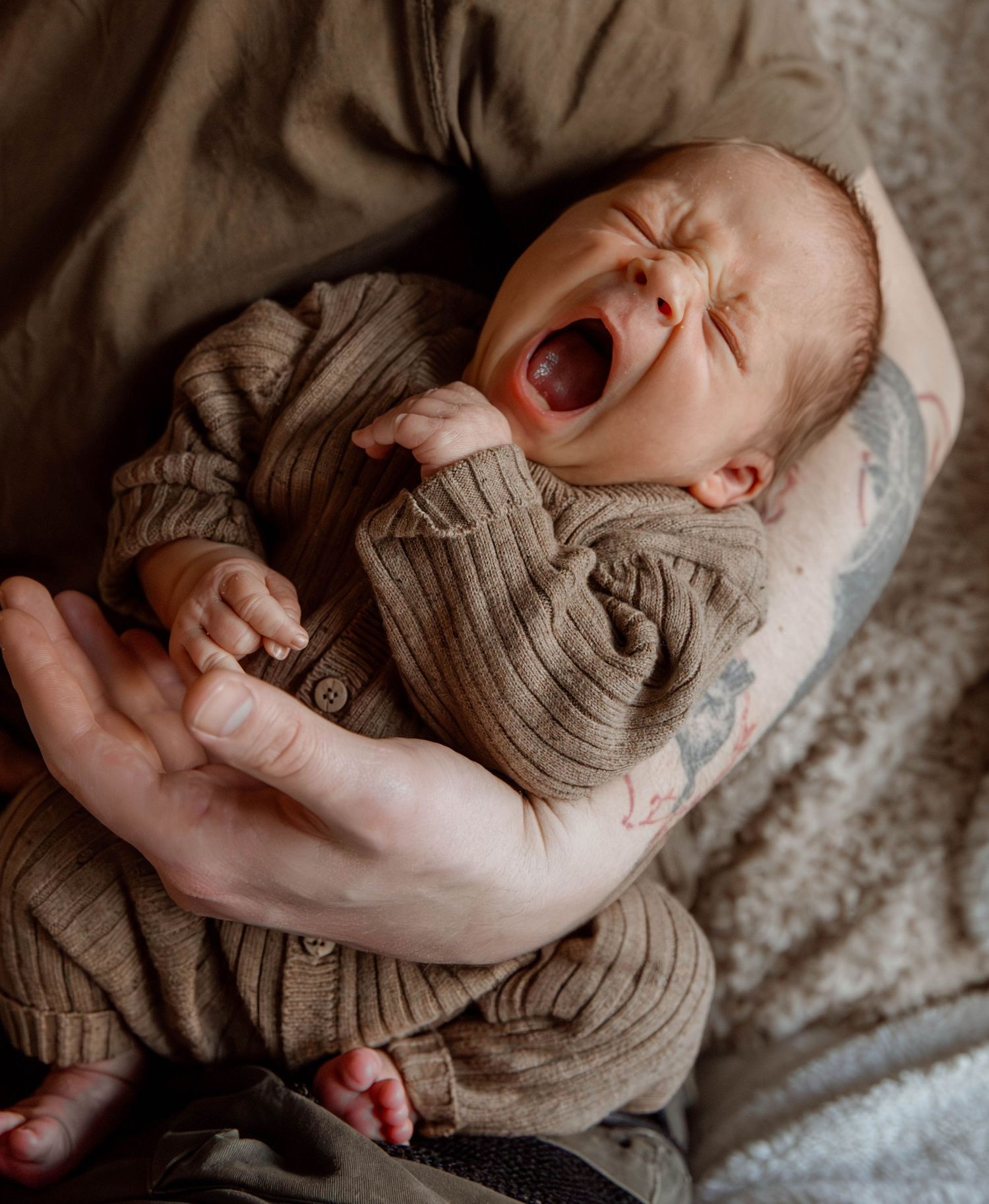 Yawning baby wearing knit sweater lying on soft blanket.