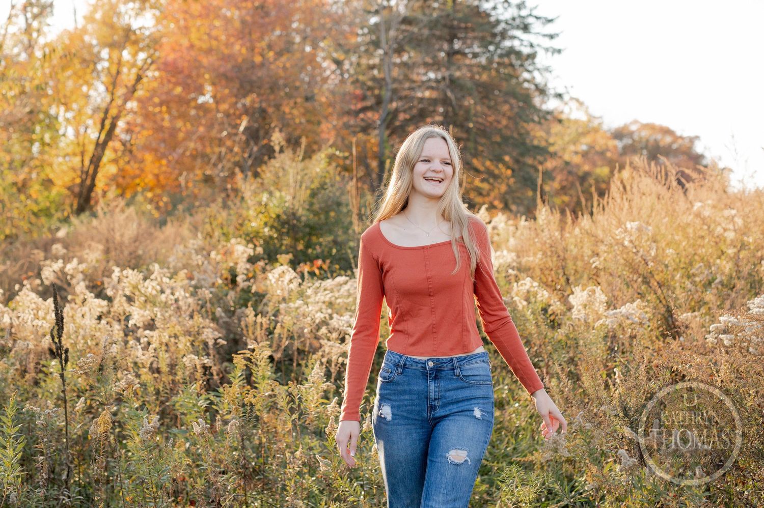 Candid autumn portrait with orange sweater and distressed jeans among fall foliage.