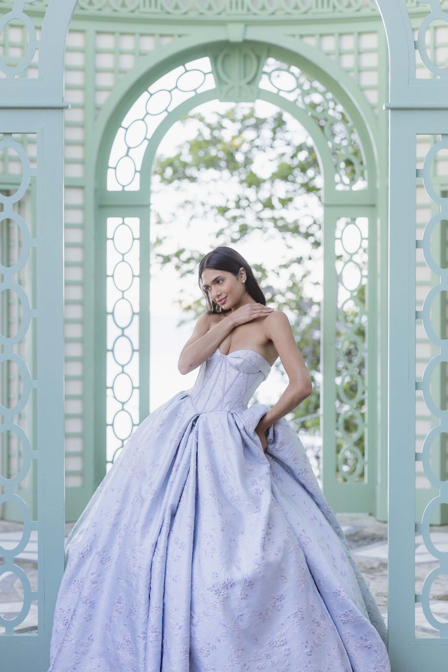 A bride in a lavender ballgown poses under an ornate mint-colored archway.