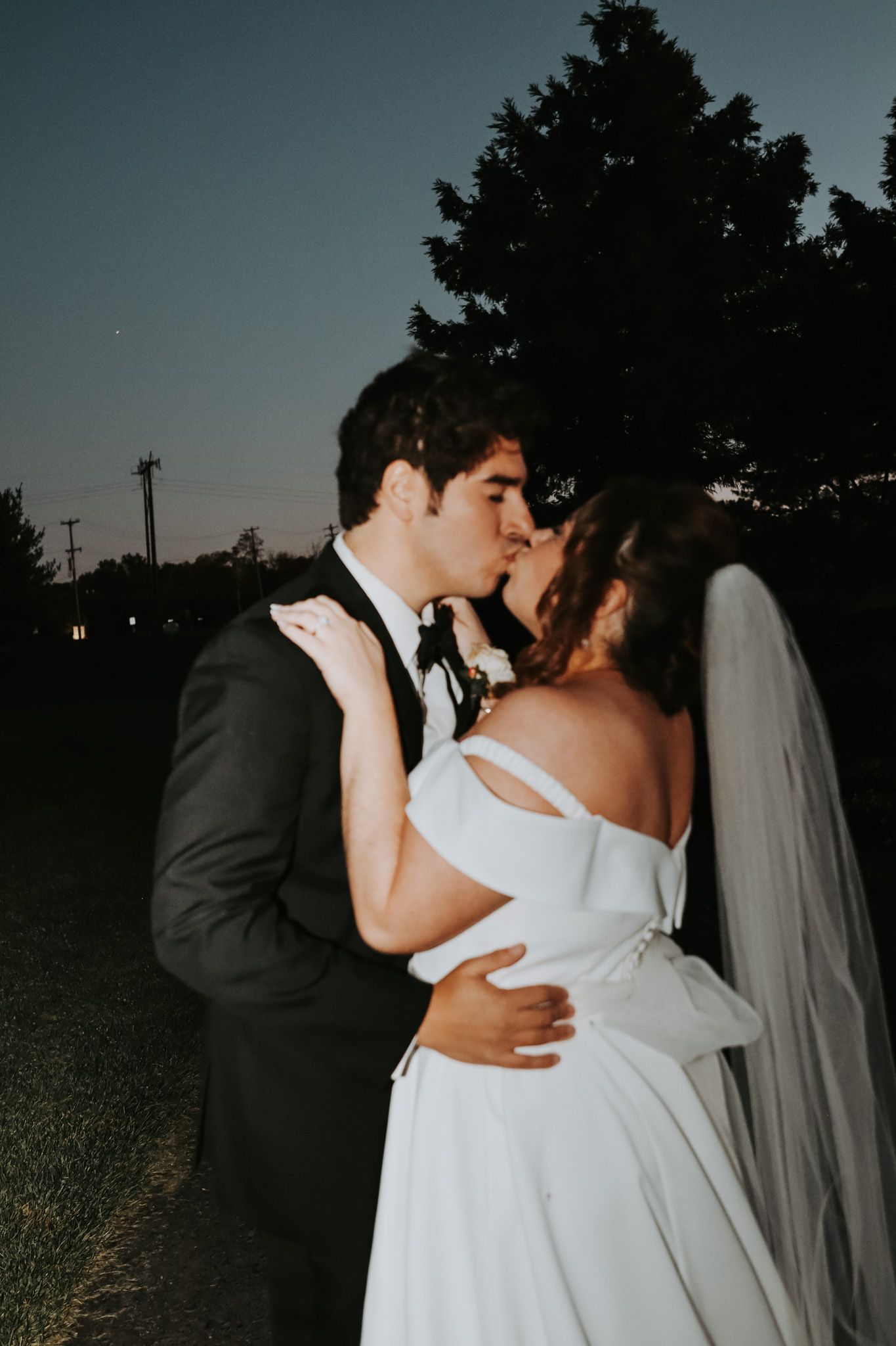 Silhouetted wedding couple embraces during twilight outdoor portrait session.